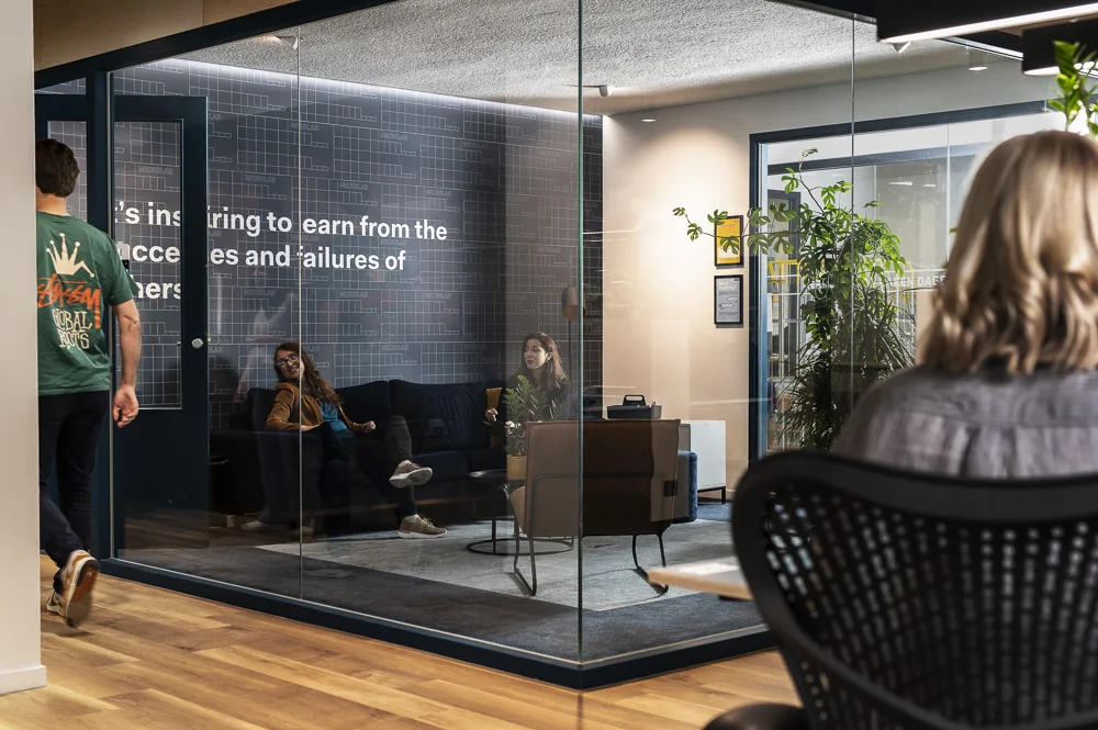 Modern kantoorinterieur aan de Aert van Nesstraat met mensen in gesprek in een glazen vergaderruimte.